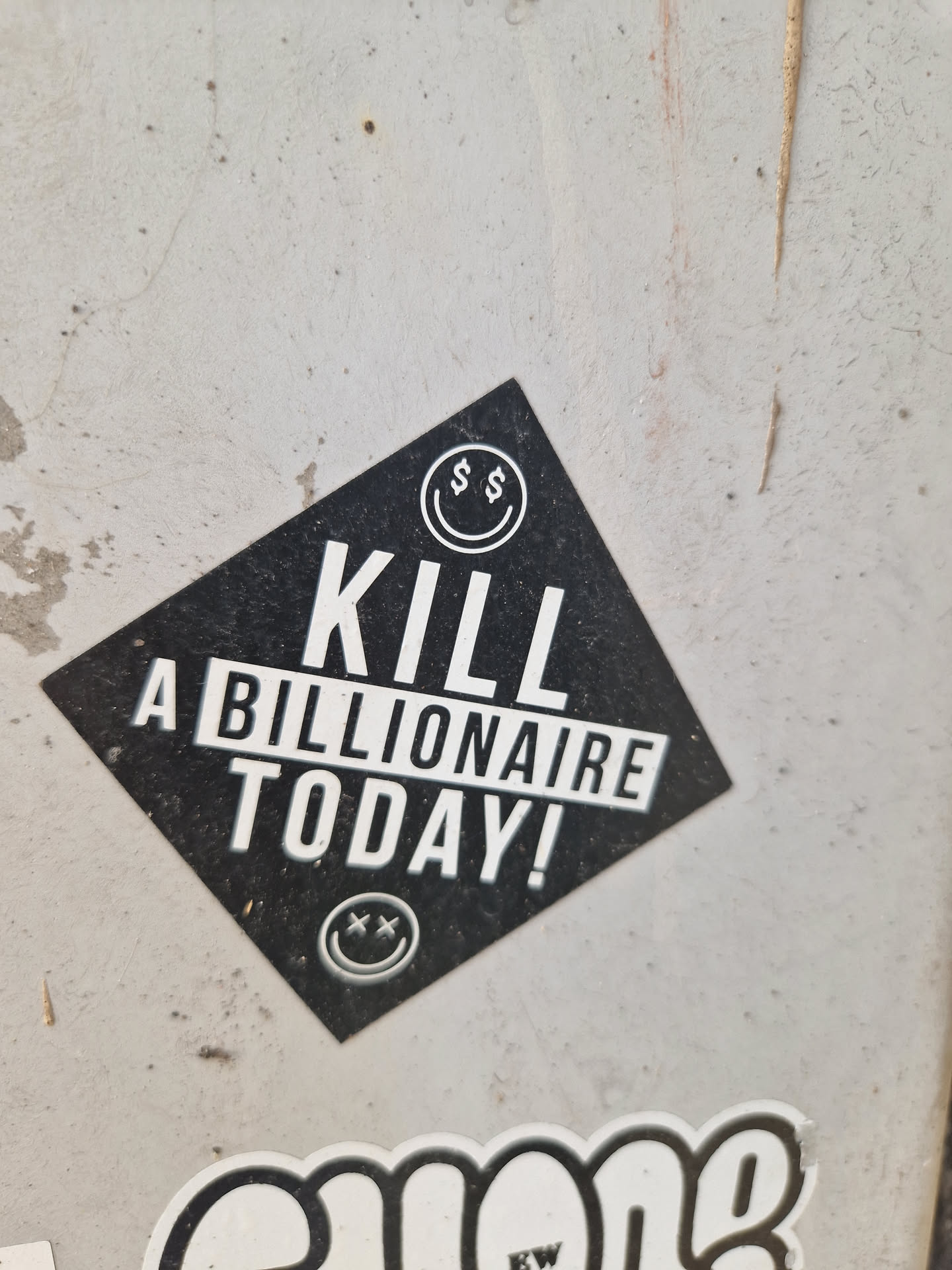 A black diamond-shaped sticker with the text "KILL A BILLIONAIRE TODAY!" in white uppercase letters. It features a smiley face with dollar signs for eyes at the top and a similar smiley face with X's for eyes at the bottom.