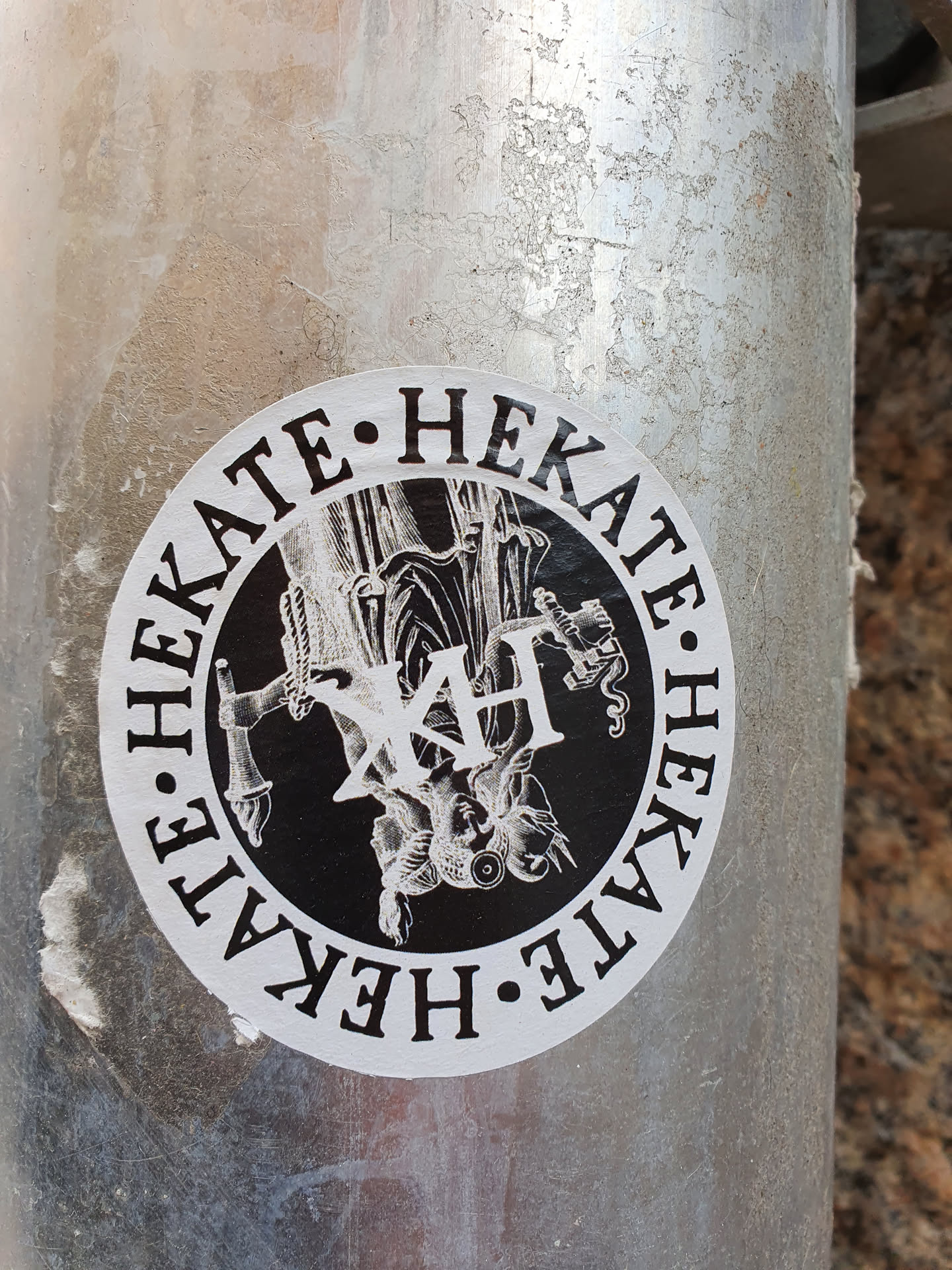Round black and white sticker featuring an illustration of Hecate, the Greek goddess of magic, witchcraft, the night, moon, ghosts, and necromancy. The sticker has the text "HEKATE" repeated around the illustration, and the initials "XH" in the center.