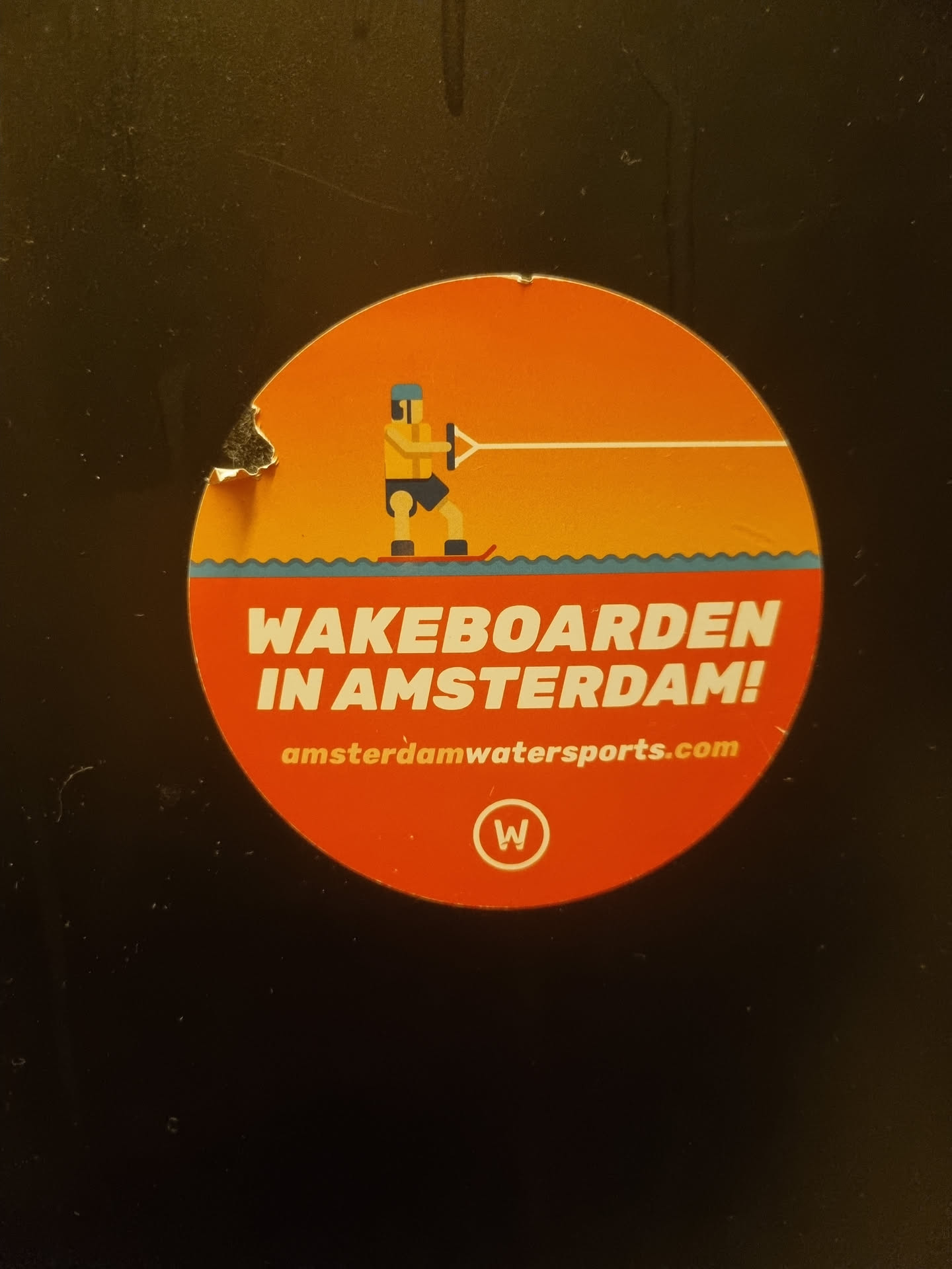 Round sticker with an illustration of a person wakeboarding. The text on the sticker says "WAKEBOARDEN IN AMSTERDAM!" and the website amsterdamwatersports.com.