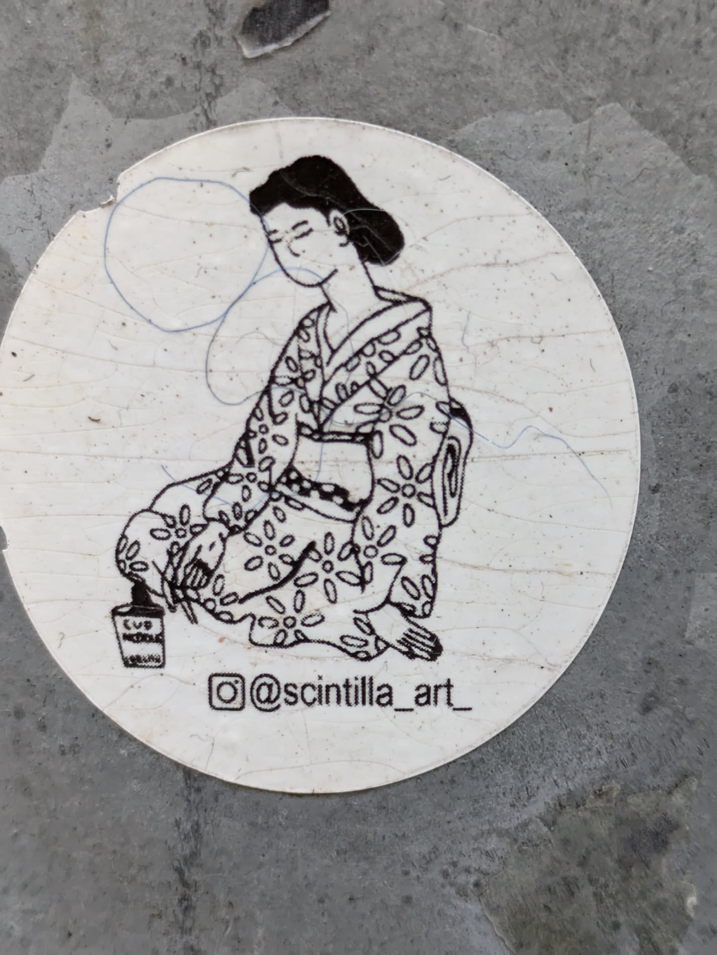 A round sticker featuring a monochrome drawing of a woman in a kimono, sitting calmly with her eyes closed.  The style is reminiscent of traditional Japanese woodblock prints.  The artist's Instagram handle is visible on the sticker. There's a small, partially visible paint can at her feet.