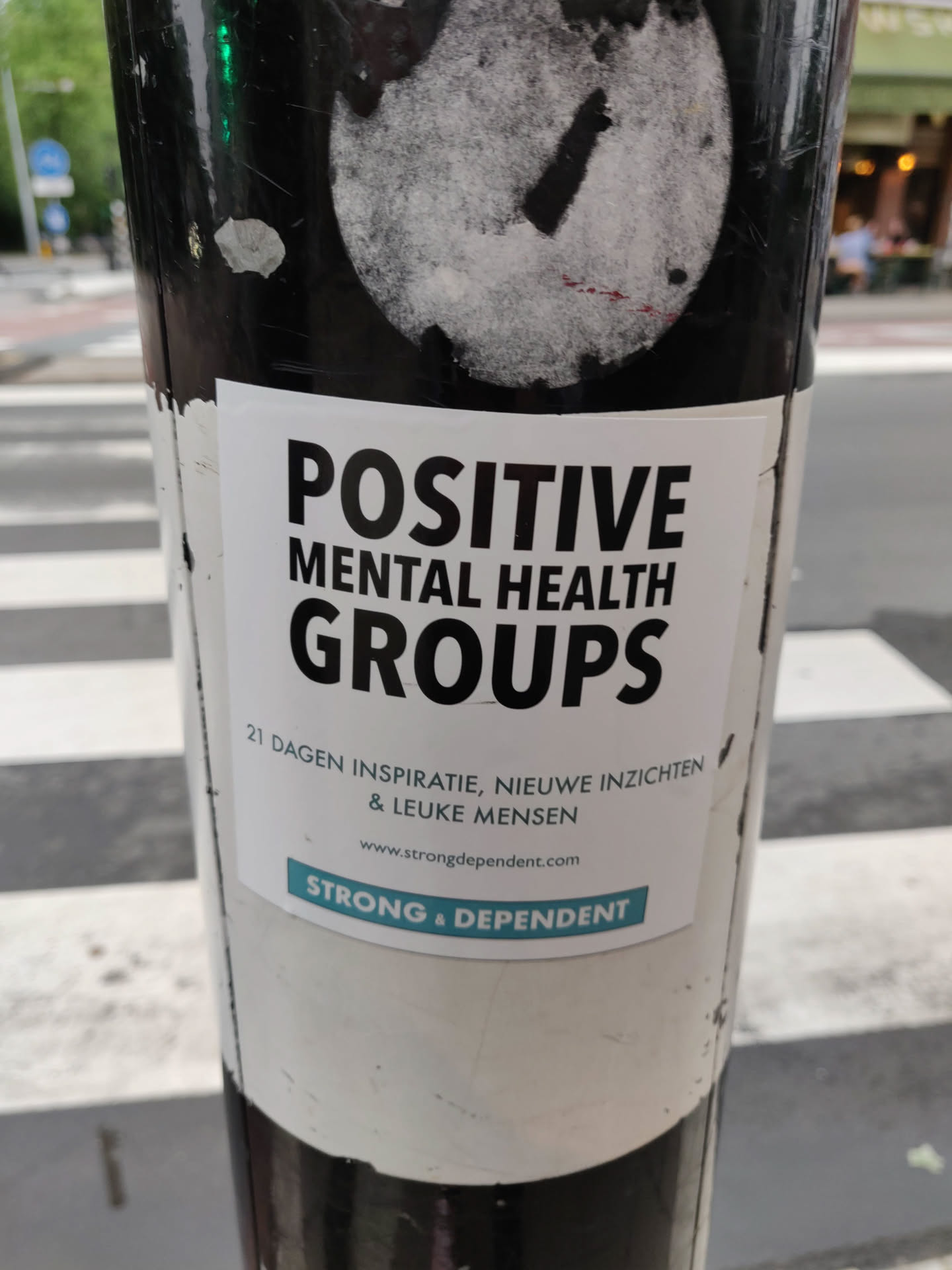 A sticker promoting positive mental health groups.  The sticker features the text "POSITIVE MENTAL HEALTH GROUPS", followed by a tagline in Dutch: "21 DAGEN INSPIRATIE, NIEUWE INZICHTEN & LEUKE MENSEN" (21 days of inspiration, new insights & nice people). A website address, www.strongdependent.com, is included along with the text "STRONG & DEPENDENT".