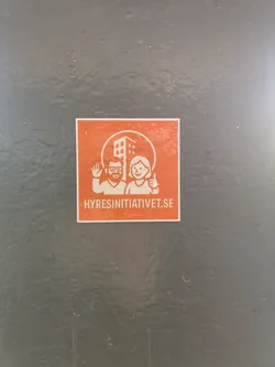 Street sticker A rectangular sticker with a vibrant orange background and white graphics. The central design features a circular frame enclosing a stylized, multi-story building. To the left of the building, a man with a beard and glasses is depicted waving, while to the right, a smiling woman gives a thumbs-up. Below this central graphic, the website address 'HYRESINITIATIVET.SE' is prominently displayed in white capital letters. The overall style is clean, friendly, and illustrative.