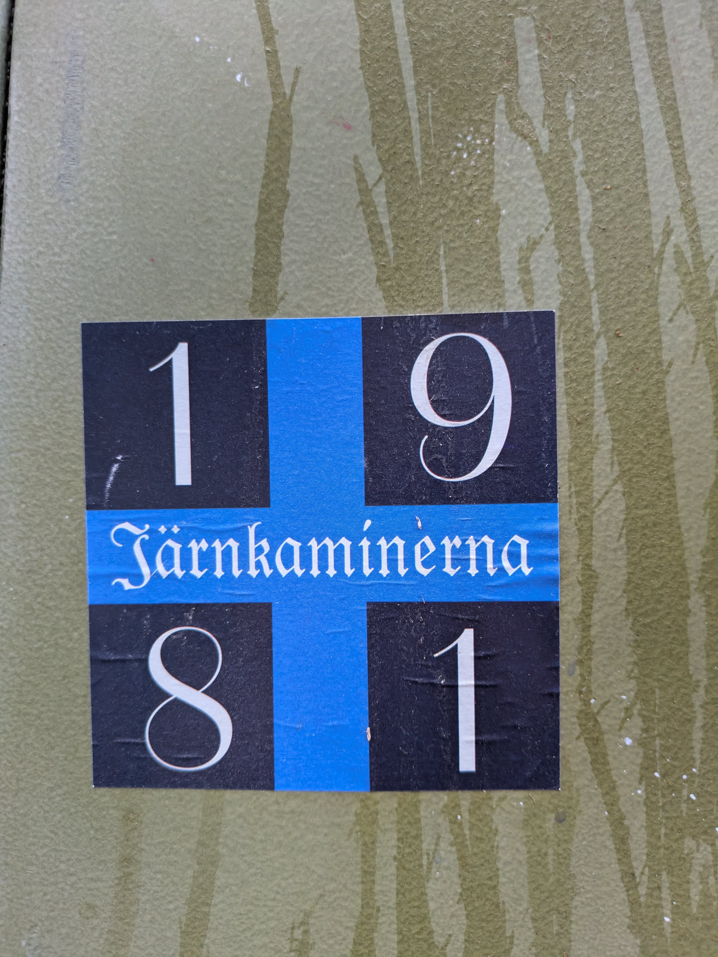 A sticker with a black and blue cross design. The numbers 1, 9, 8, and 1 are in the corners of the cross. The word "Jarnkaminerna" is in the middle.