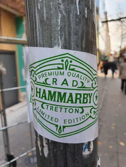 A green and white sticker with the text 'Premium Quality Craft Hammarby Tretton Limited Edition' and a unique design. It's a limited edition item, suggesting exclusivity. The sticker is affixed to a metal pole outdoors.