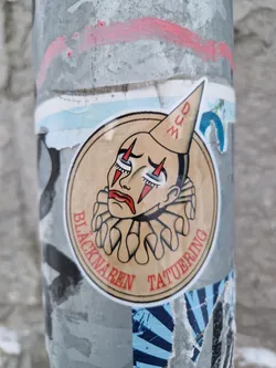 Round sticker featuring a vintage-style illustration of a sad clown wearing a dunce cap. The text around the illustration says "Blacknaren Tatuering." 