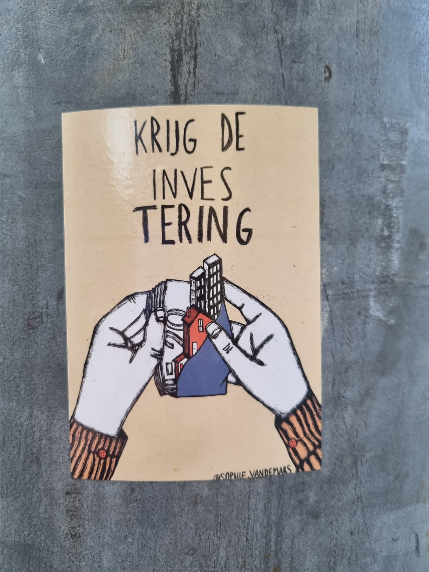 A sticker with a drawing of two hands holding a small model of houses and buildings. The text on the sticker says "KRIJG DE INVES TERING" which translates to "Get the investment" in Dutch. The artist's signature is visible at the bottom.