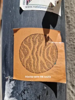 Orange square sticker with a black and white circular design. The text 'Coated with the Sauce' is printed at the bottom of the sticker.