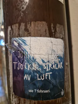 A worn-out sticker announcing an event: John Ljebø - Tjocka strålar av luft.  The date is visible: ute 7 februari (7th of February). The sticker shows some damage and weathering.