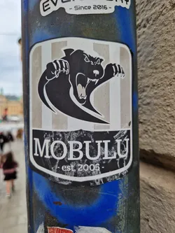 A sticker featuring a black panther-like creature with claws outstretched. The background is light grey with vertical stripes.  The text 'MOBULU' is prominently displayed below the creature, with '- est 2005 -' underneath.