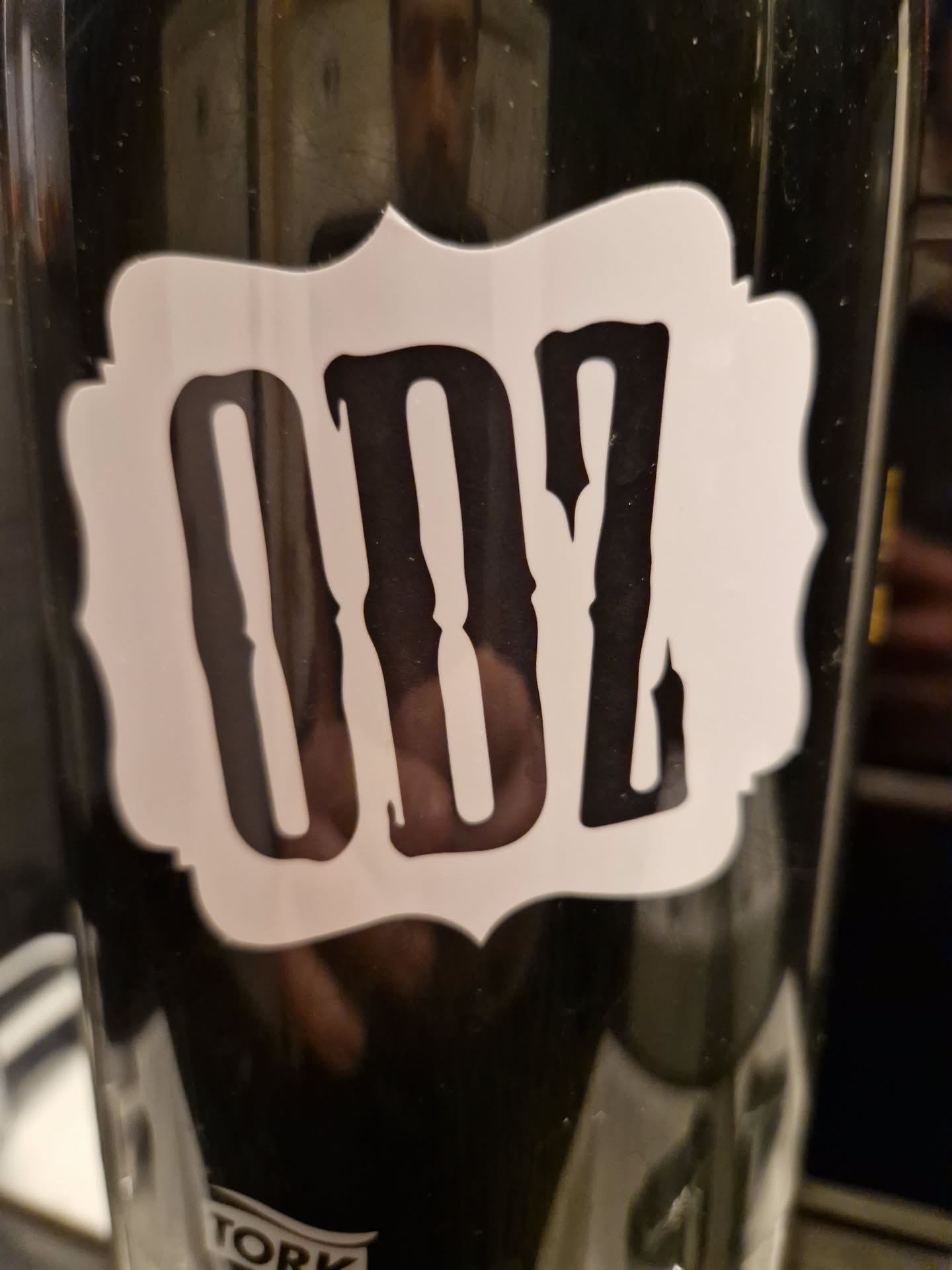 A black and white sticker with the letters ODZ in a stylized font. The sticker is rectangular with slightly curved edges and is placed on a dark surface.