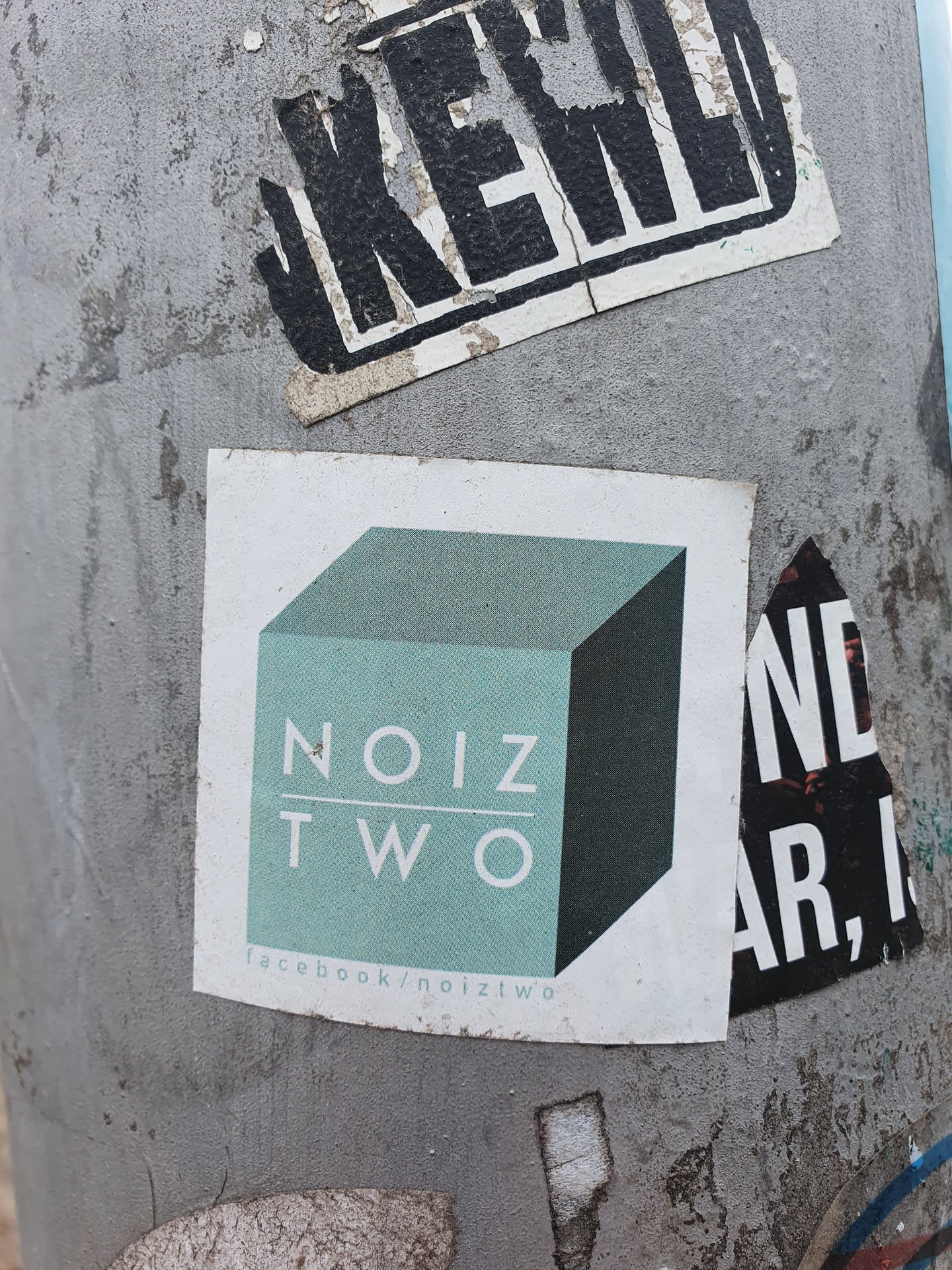 A minimalist sticker featuring the logo of Noiz Two, a teal cube with the text 'NOIZ TWO' in a sans-serif font.  The sticker also includes a Facebook link at the bottom.