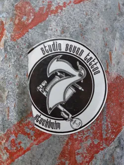 Black and white sticker with an illustration of a tattoo machine and the text "Studio Seven Tattoo Stockholm".