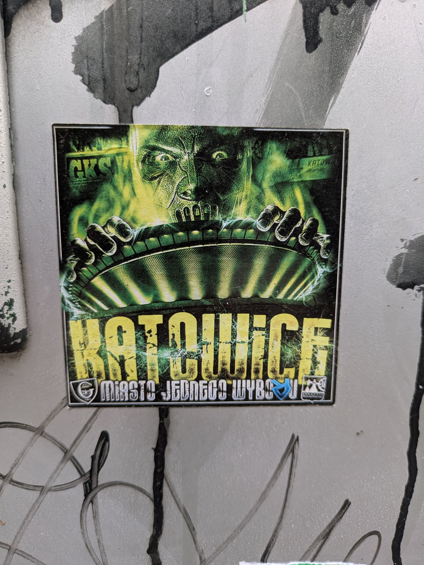 This sticker features a menacing figure with glowing green eyes and hands gripping a disc. The text "KATOWICE" is prominently displayed in yellow, with the phrase "MIASTO JEDNEGO WYBORU" below. The GKS logo is visible in the top left corner.