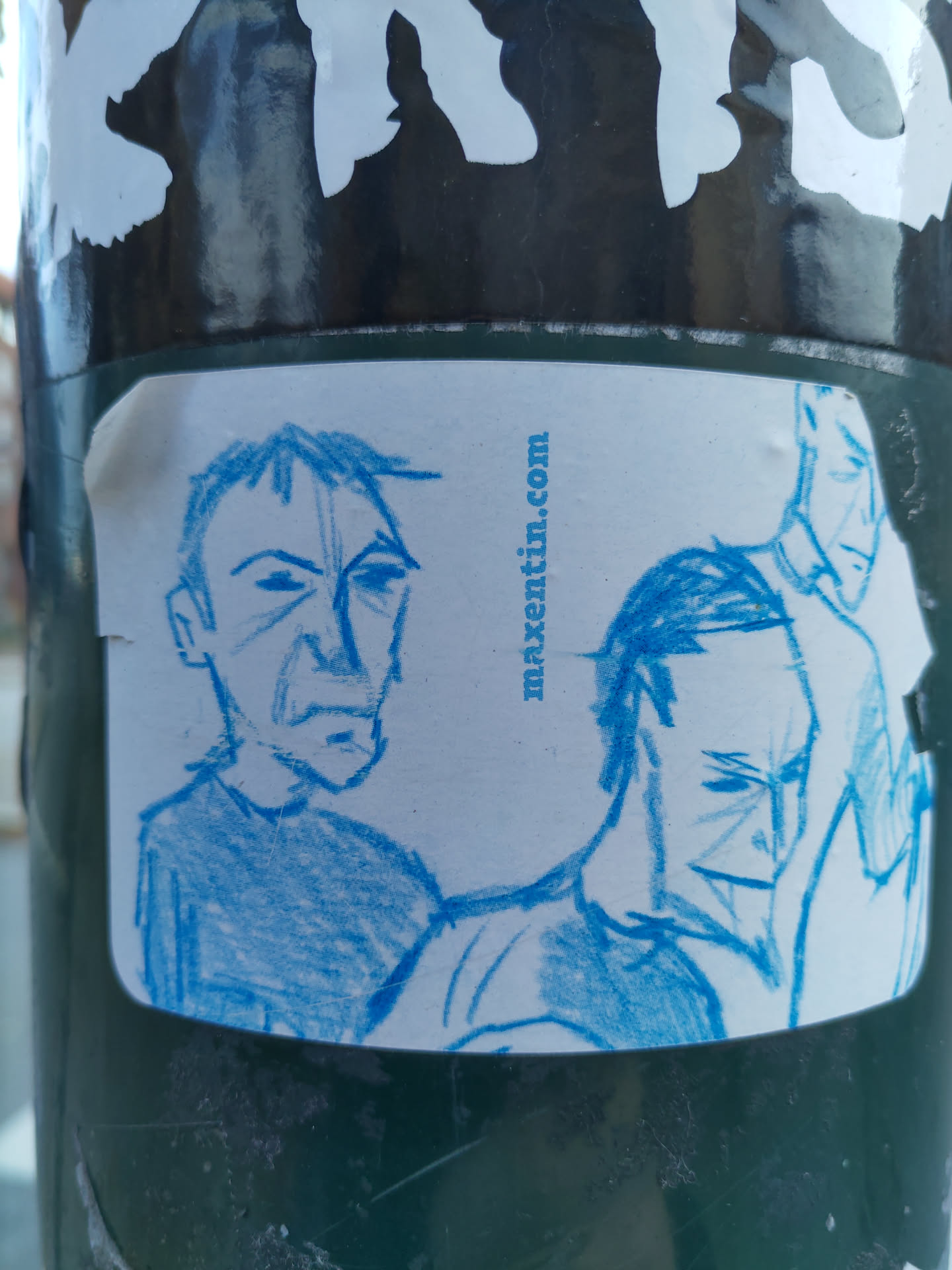A sticker with a light blue hand drawing of three men's faces. The style is simple and slightly sketchy.  A website address, maxtentin.com, is printed at the top right.