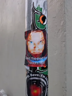 Street sticker A rectangular glossy sticker featuring a close-up still of Dr. David Bowman (portrayed by Keir Dullea) wearing a red spacesuit helmet from the film '2001: A Space Odyssey'. His face is illuminated from below, highlighting his intense gaze and bright blue eyes. Across the lower portion of his visor and suit collar, the famous quote 'Open the pod bay doors Hal!' is printed in clean, white sans-serif text with a subtle dark outline.