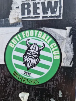 A round green and white sticker with a viking logo in the center. The text "Buti Football Club" is written in a circle around the logo, and the text "Warriors 2013" is written below the logo.