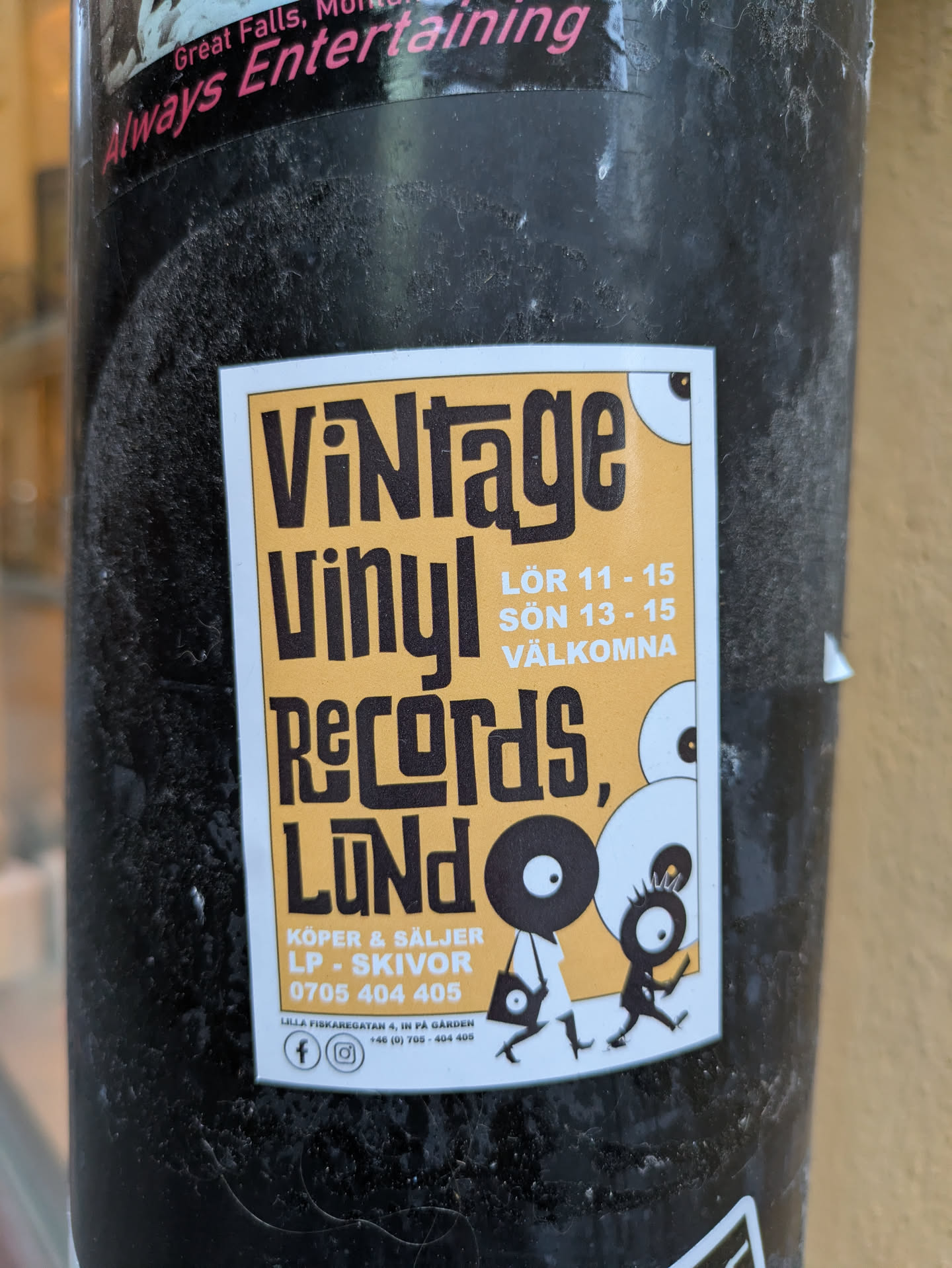 A sticker advertising Vintage Vinyl Records in Lund, Sweden.  The sticker features illustrations of two figures carrying vinyl records and indicates that they buy and sell LPs and records. Contact information is included.