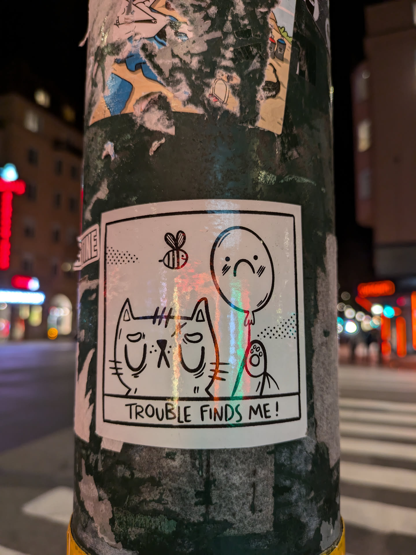 A sticker featuring a cartoon cat with a grumpy expression, a sad balloon, and a bee. The text below the illustration says "Trouble finds me!"