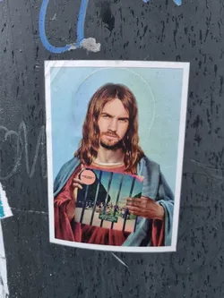 A sticker depicting Jesus Christ holding what seems to be Tame Impala's album cover behind bars. The sticker has a slightly vintage or retro feel.