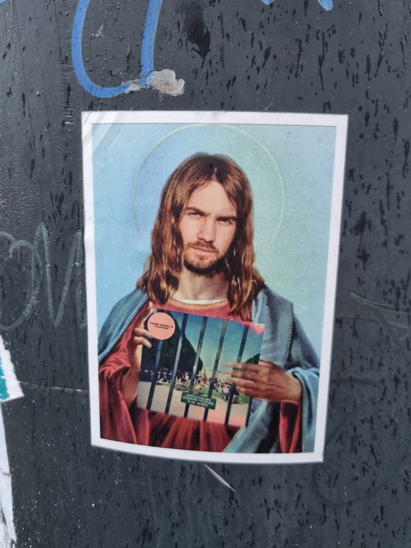 A sticker depicting Jesus Christ holding what seems to be Tame Impala's album cover behind bars. The sticker has a slightly vintage or retro feel.