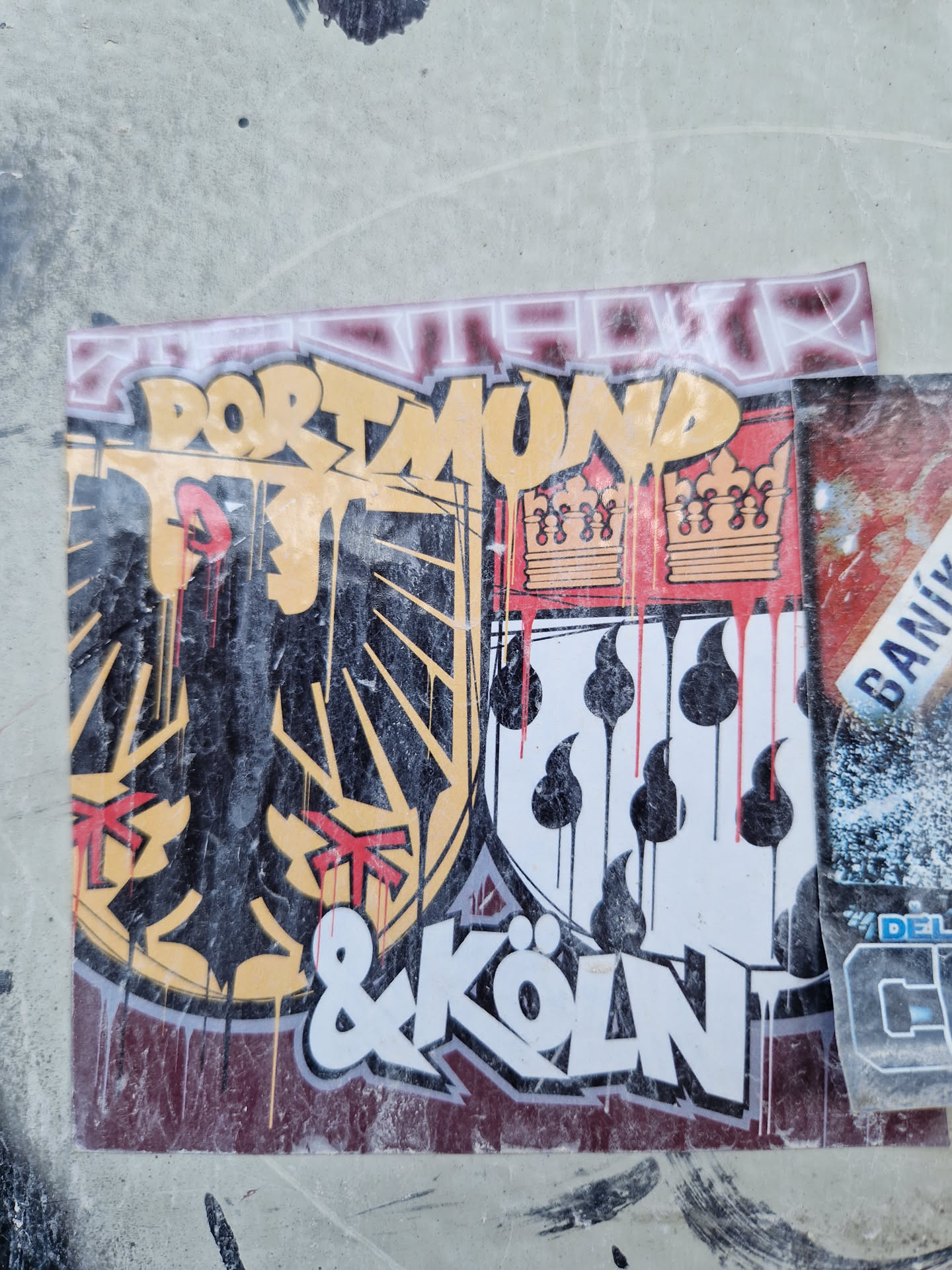 A sticker featuring a graffiti-style design combining the coats of arms of Dortmund and Cologne, Germany.  The design includes stylized text and drips, giving it a street art aesthetic.