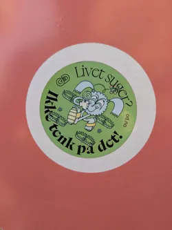 This is a circular sticker with a white outer border and a light green background. The central illustration features a whimsical, fluffy creature, possibly a sheep or a cloud-like being, with light blue and white fur, wearing yellow sandals, and holding a red and white swirl lollipop. Several open bear traps are depicted around the creature's feet. The text "Livet suger?" (Life sucks?) is curved along the top, and "Ikke tenk på det!" (Don't think about it!) is curved along the bottom, both in black lettering. On the right side, oriented vertically, is the web address "od.no". The background includes subtle wavy lines and small floral elements.