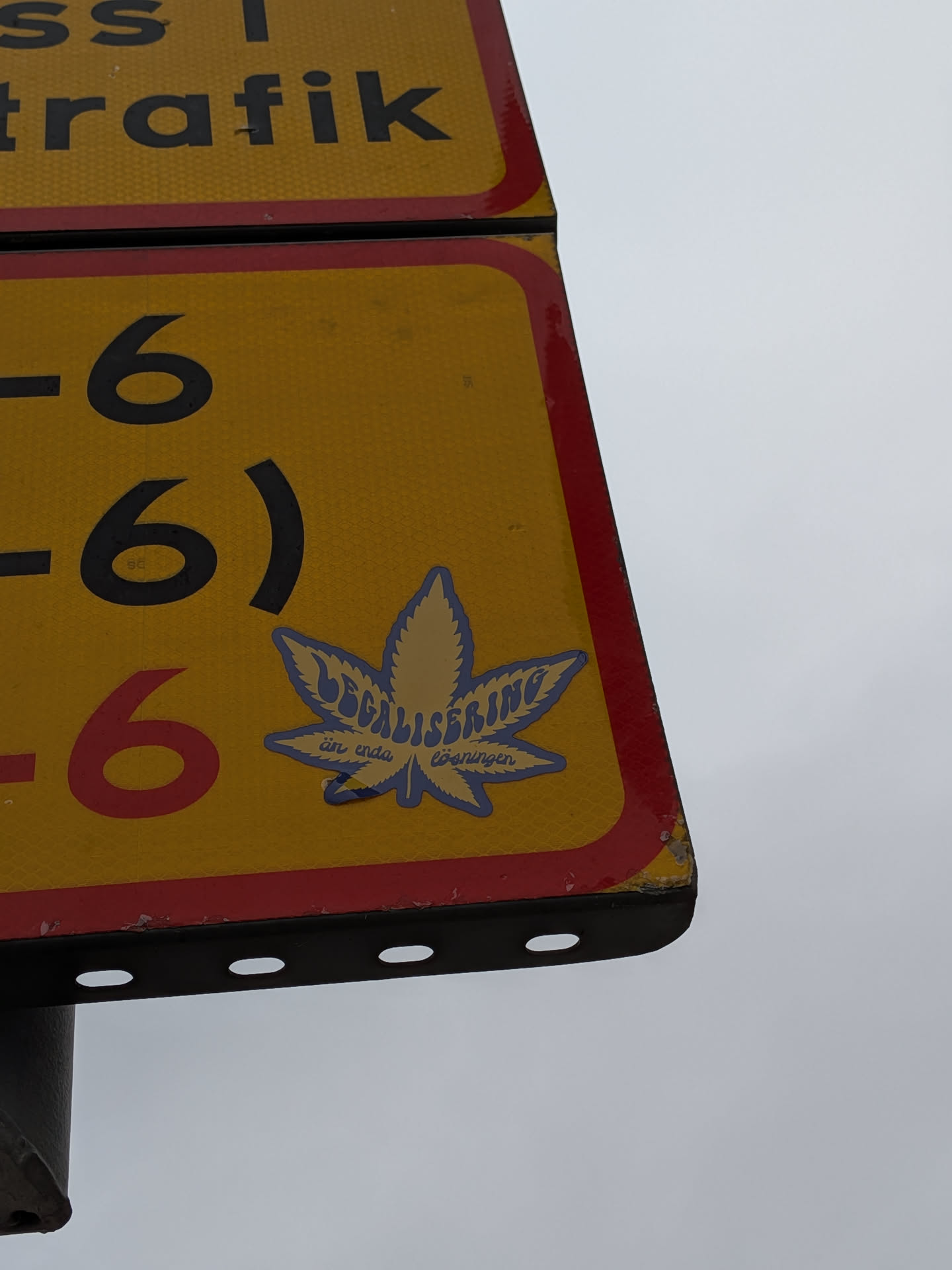 The sticker is shaped like a cannabis leaf and is predominantly blue with yellow lettering. The text 'LEGALISERING' is prominently displayed in a stylized font across the leaf. Below this, in smaller text, it reads 'än enda lösningen'. The sticker has a slightly glossy finish and appears to be adhered to a yellow traffic sign with red borders.