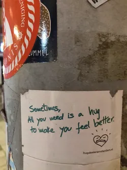 A heartwarming sticker with a simple message promoting the power of hugs.  It features a small drawing of two figures embracing within a heart shape and includes a website address.