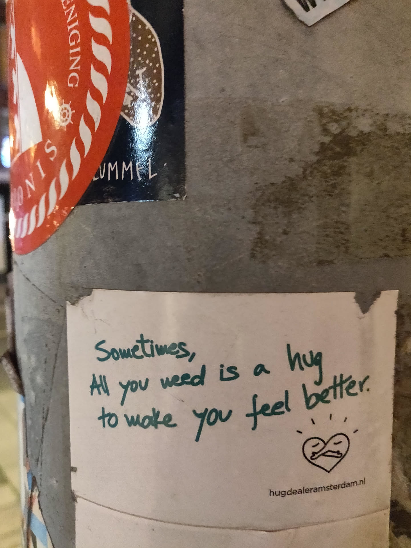 A heartwarming sticker with a simple message promoting the power of hugs.  It features a small drawing of two figures embracing within a heart shape and includes a website address.