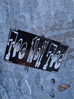 A black and white sticker with the text "The Well Free" in a stylized font. The sticker is affixed to a gray, textured surface.  The text "OLYDIG.ET" appears in smaller print in the corners.