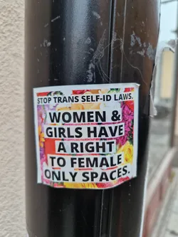 A sticker with a floral design advocating for women's rights and against trans self-ID laws. The sticker features bold text on a background of colorful flowers.