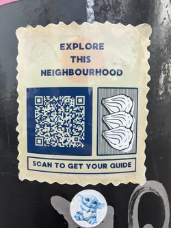 A sticker with a QR code that leads to a neighbourhood guide and an illustration of oysters. The sticker has a vintage postage stamp design.