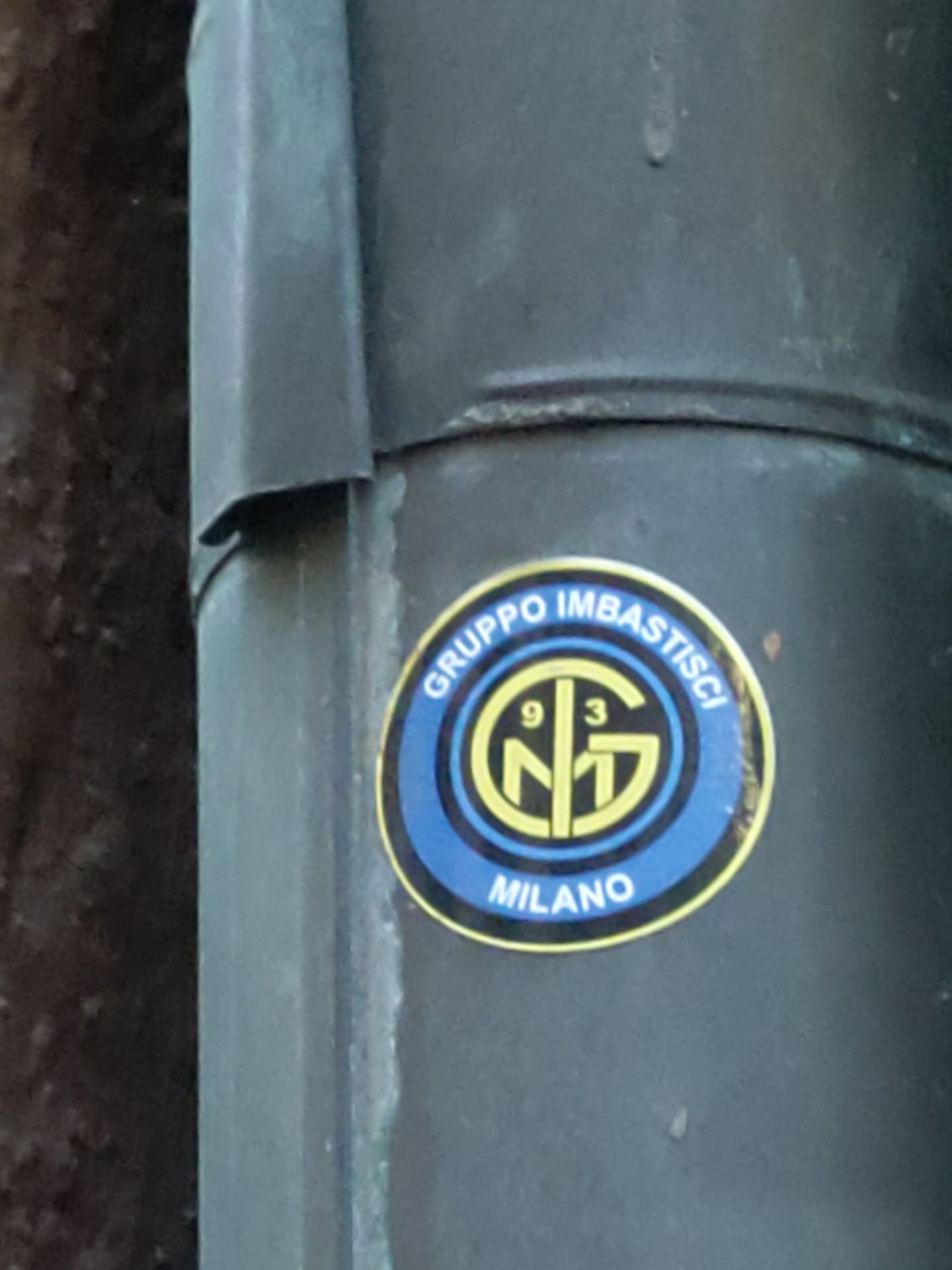 A round sticker with a logo featuring the letters 'NG' intertwined, the number '93', and the word 'MILANO' at the bottom. The logo is in yellow and gold, and it is set against a blue background. The text 'GRUPPO IMBASTISCI' is printed above the logo.