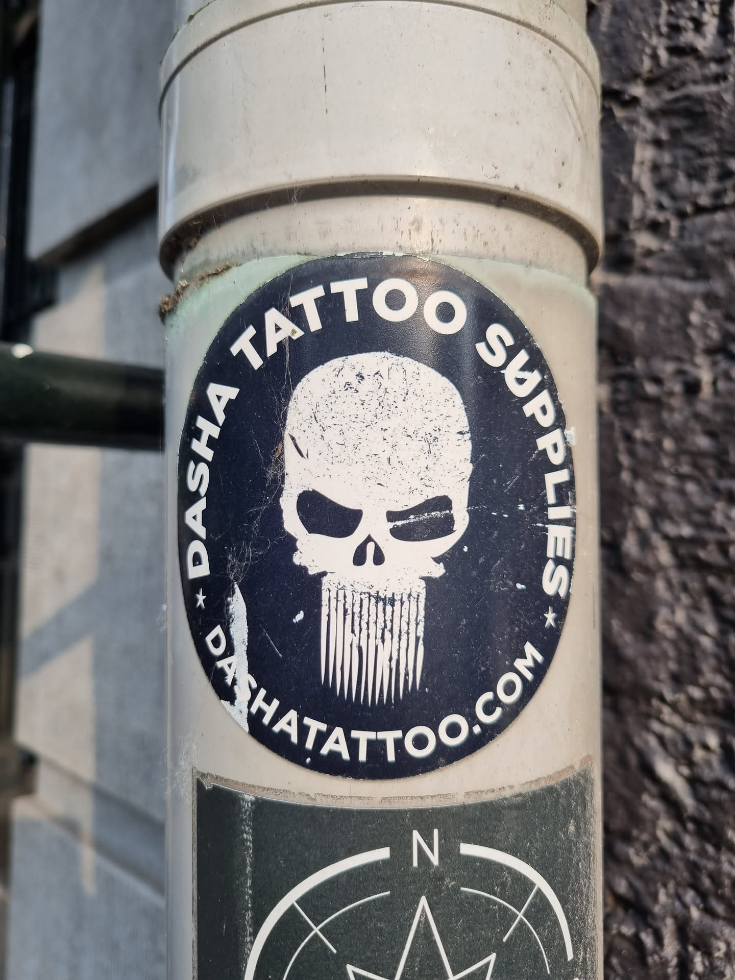 A round sticker with the text "DASHA TATTOO SUPPLIES" encircling a skull graphic with a beard. The website dashatattoo.com is also visible. The sticker is affixed to a pipe.
