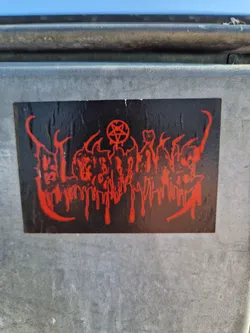 A black and red sticker with a design that appears to be inspired by occult or metal music imagery.  The sticker features dripping red elements and a pentagram. The text is illegible.