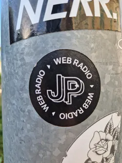 Black and white circular sticker with the letters JP in the center and the text "WEB RADIO" repeated around the circle. 