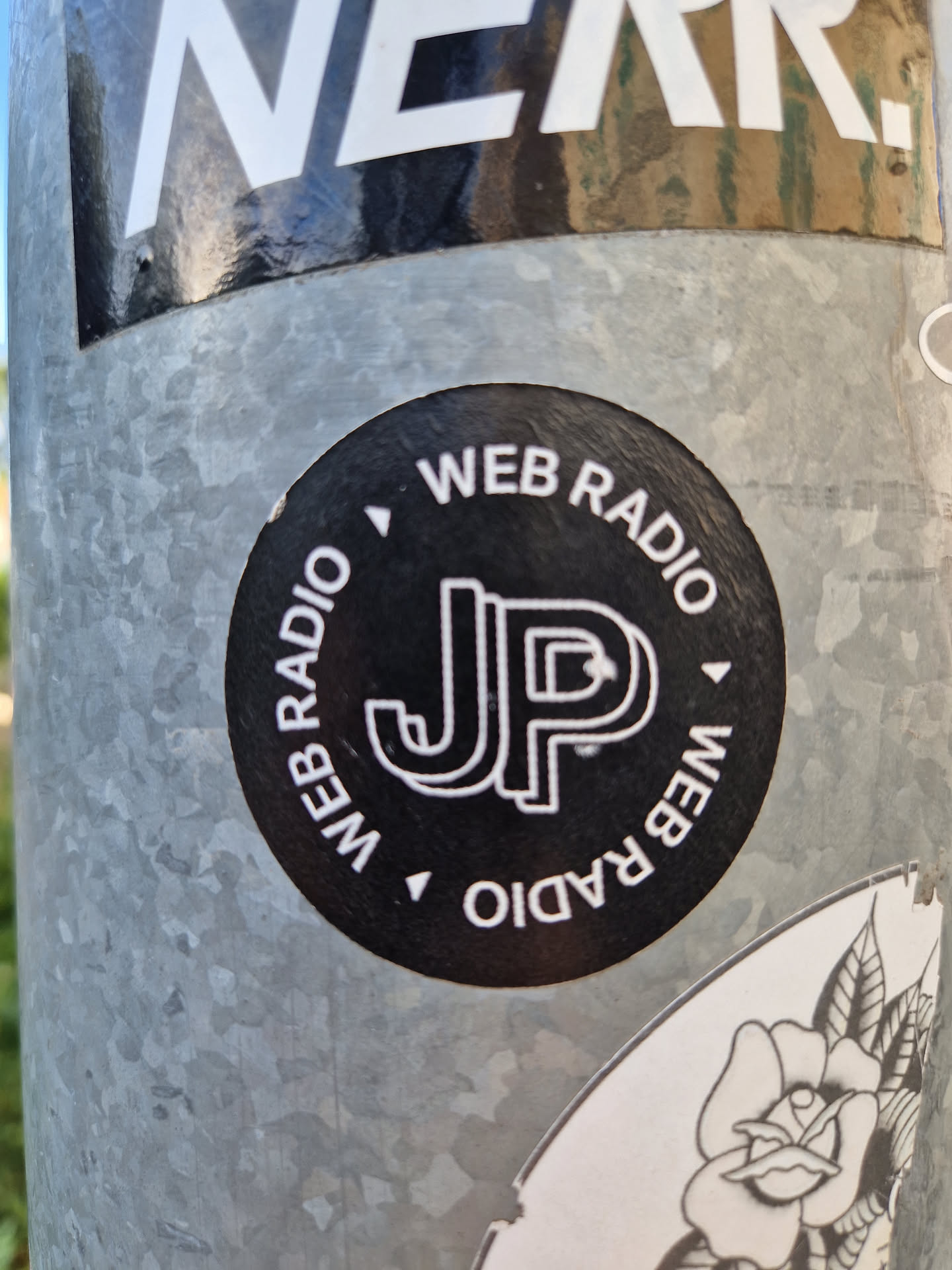 Black and white circular sticker with the letters JP in the center and the text "WEB RADIO" repeated around the circle. 