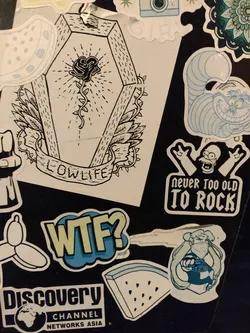 A sticker with a black line drawing of a rose in a coffin. The words "LOWLIFE" are written on a banner below the coffin. The style is reminiscent of traditional tattoo art.