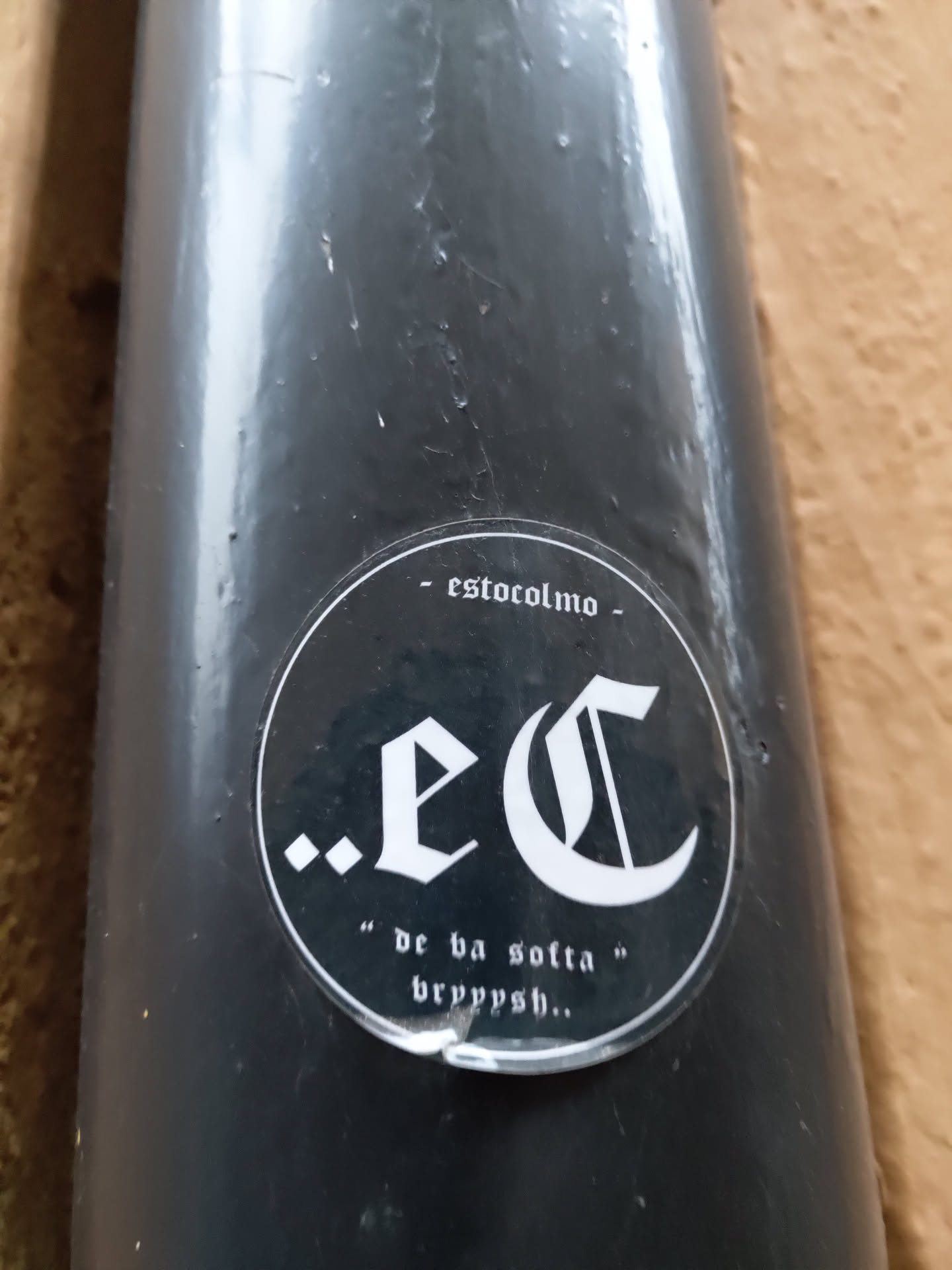 A black and white circular sticker with the letters '.eC' in a gothic-style font.  Below it says "de ba sotla" bryppysh... in a smaller font. At the top, it says '- estocolmo -'. The sticker is applied to a dark gray cylindrical object.