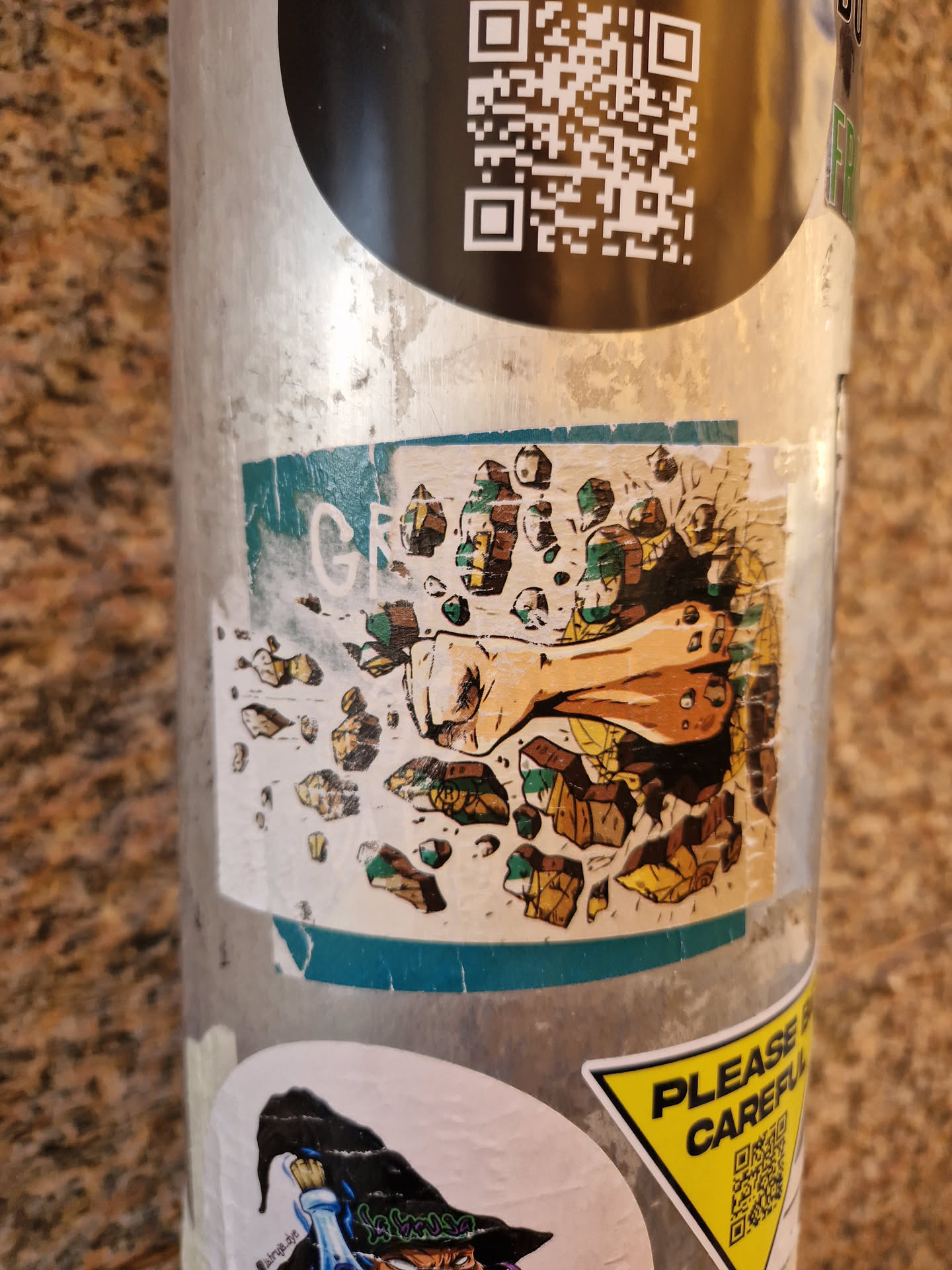 A sticker featuring a stylized illustration of a powerful fist shattering stone. The art style is reminiscent of comic books or graphic novels, with bold lines and vibrant colors. The sticker is affixed to a metal pole, likely in an outdoor urban setting.