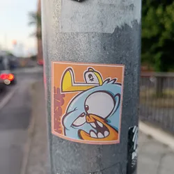 This sticker features a light blue bird with a large eye and a mischievous expression.  It's wearing a yellow hat with a small skull on it and is set against an orange background. The style is reminiscent of graffiti or street art.