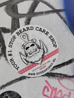 A round sticker with a illustration of a bearded man's face with an anchor. It says "Your #1 Stop Beard Care Shop" and has a website and discount code.