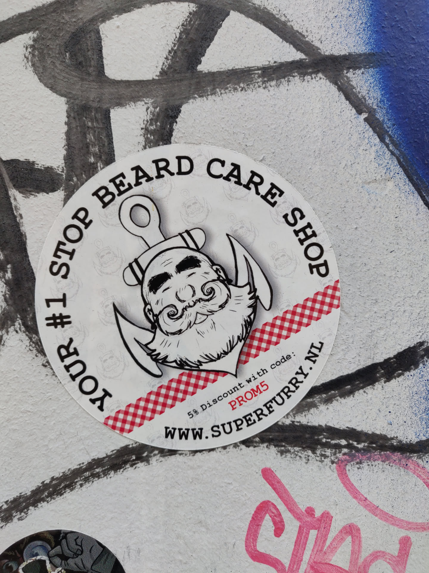 A round sticker with a illustration of a bearded man's face with an anchor. It says "Your #1 Stop Beard Care Shop" and has a website and discount code.
