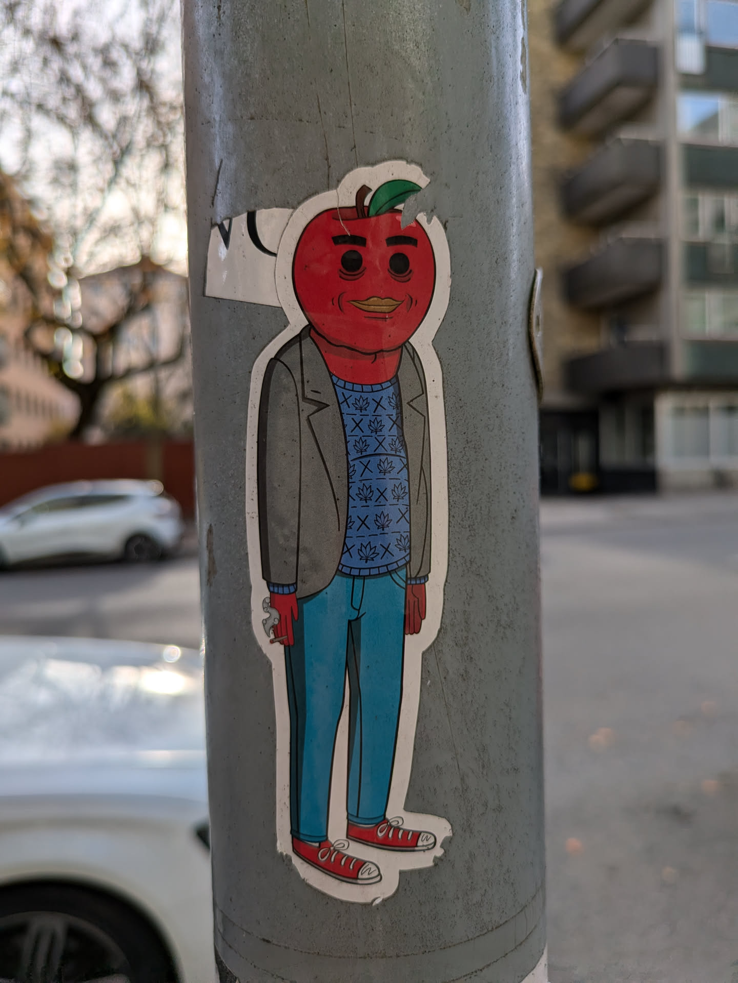 A sticker featuring an anthropomorphic apple character wearing a gray jacket, blue jeans, and red sneakers.  The apple head has a smirk and simple eyes. The design is simple and cartoonish.