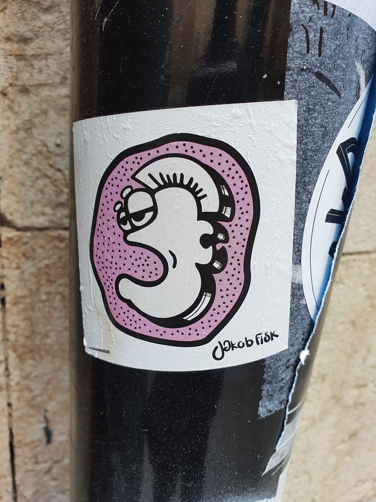 A quirky character with a mohawk, encased in a pink dotted circle. The sticker has a hand-drawn aesthetic and is signed by the artist.