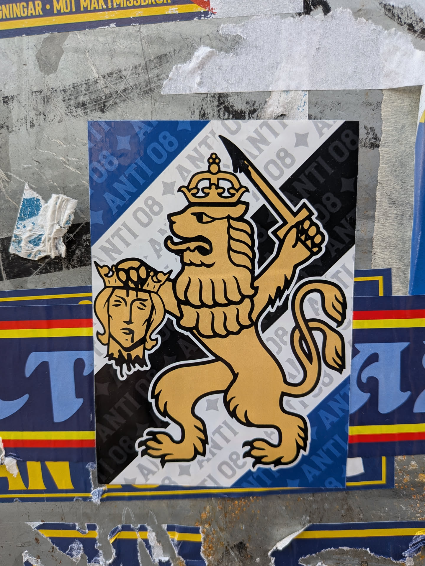 The sticker features a stylized golden lion in a rampant pose, holding a sword aloft in its right paw and a severed, crowned head in its left. The lion has a mane, a curled tail, and is depicted with sharp claws. The background is divided diagonally into sections of blue with white stars and the text 'ANTI 08', and white with grey stars and the text 'ANTI 08'. The overall design is bold and graphic, with thick black outlines.