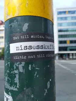 A sticker on a pole with text in Swedish.  The text translates roughly to: "Food for school, made with nissesskaffe. Real food for real people."
