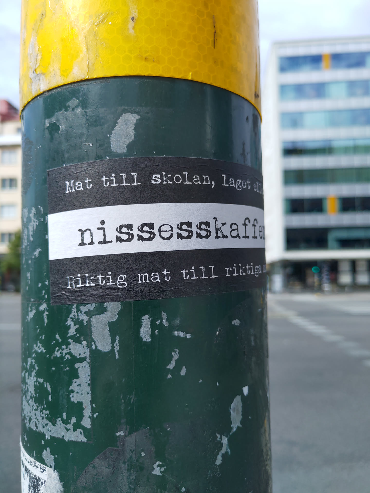 A sticker on a pole with text in Swedish.  The text translates roughly to: "Food for school, made with nissesskaffe. Real food for real people."