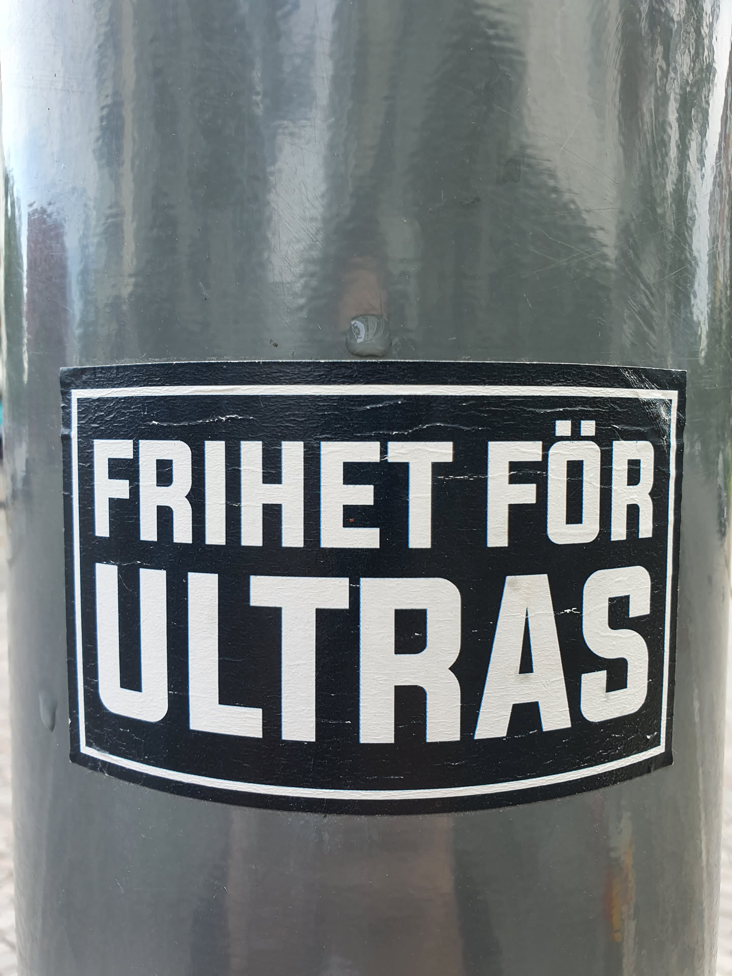 A black and white sticker with the text "FRIHET FÖR ULTRAS" on a gray surface. The sticker shows some wear and tear.