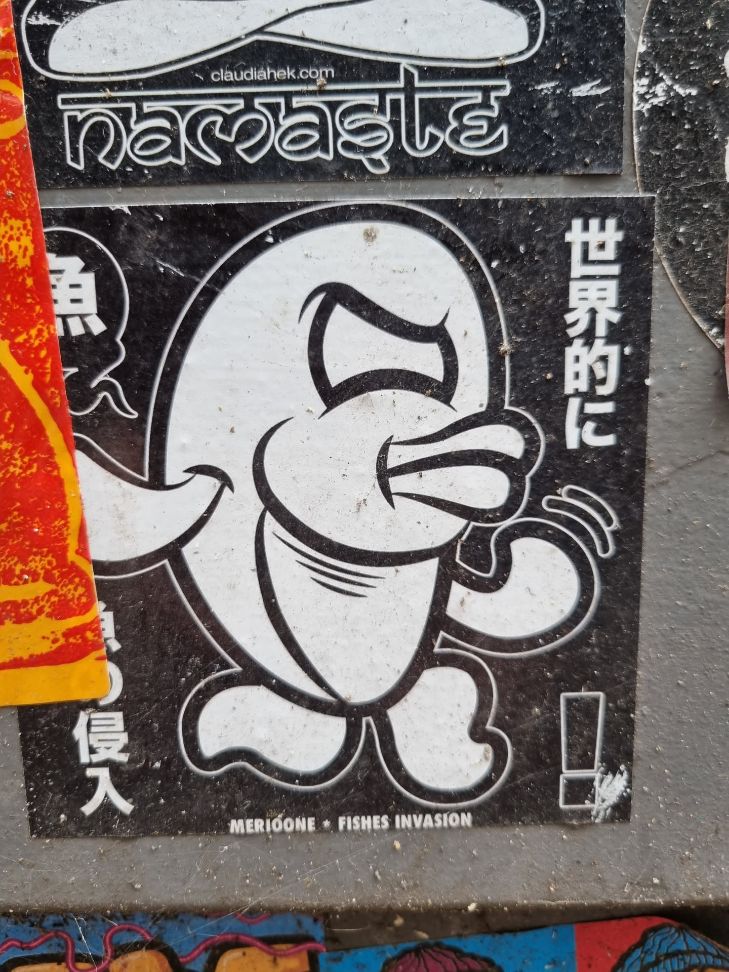 Black and white sticker of a cartoon fish character with a grumpy expression. The sticker has Japanese text on it and the words  "Merioone Fishes Invasion" at the bottom. 